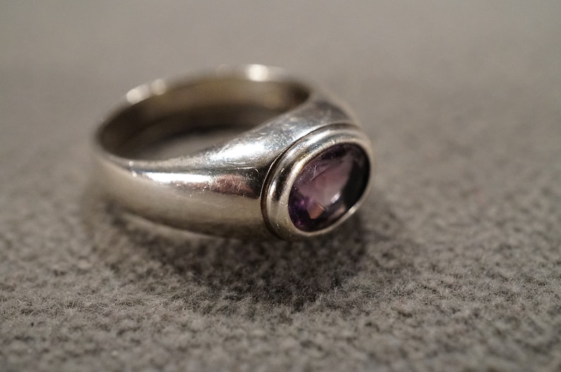 May include: A silver ring with a bezel setting featuring a purple amethyst gemstone.