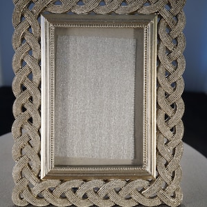 May include: A gold picture frame with a braided design. The frame is empty and ready for a photo.