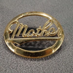 May include: Gold-toned metal brooch with the word "Mother" in a cursive script.