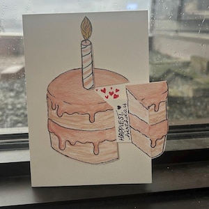 May include: Hand-drawn birthday card showing a two-tier cake with a slice removed. The cake is brown with darker brown icing drips. A lit candle is on top. The words "Happiest Birthday" are on the slice, with red hearts.