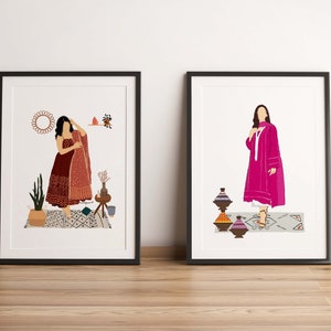 May include: Two framed art prints. One features a woman in a maroon dress with a patterned shawl. The other shows a woman in a pink outfit. Both prints have a minimalist style with decorative elements.