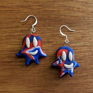Op de afbeelding: Een paar blauwe, rode en witte spookvormige oorbellen met een wit lachend gezicht. De oorbellen hebben zilveren haakjes.