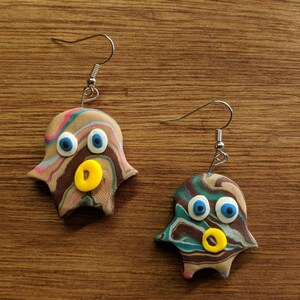Op de afbeelding: Een paar bruine, groene en blauwe swirl-geestoorbellen met gele en blauwe ogen en een gele mond. De oorbellen zijn gemaakt van polymer clay en hebben zilveren haakjes.