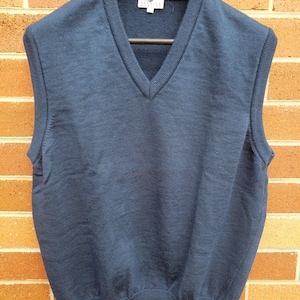 May include: A navy blue V-neck knitted sweater vest. The sleeveless top is displayed on a black hanger. The vest features a ribbed hem and a small label near the neckline. The garment is a classic style.