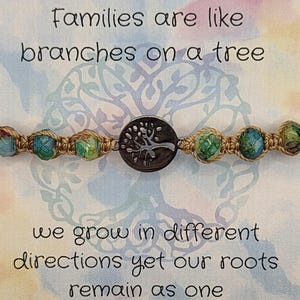 May include: A macrame bracelet with blue and green beads and a silver-colored tree charm. The background features text that reads "Families are like branches on a tree" and "we grow in different directions yet our roots remain as one."