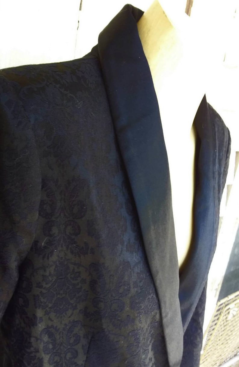 May include: A black blazer with a satin collar. The blazer has a floral pattern.