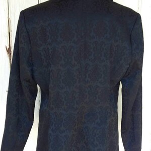 May include: A black blazer with a damask pattern. The blazer has a notched collar and long sleeves.