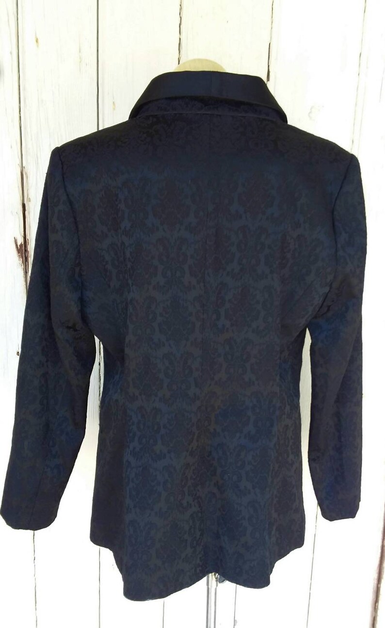 May include: A black blazer with a damask pattern. The blazer has a notched collar and long sleeves.