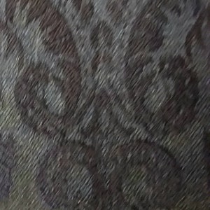 May include: A close-up of a grey and brown patterned fabric with a subtle sheen. The fabric has a textured, woven appearance.