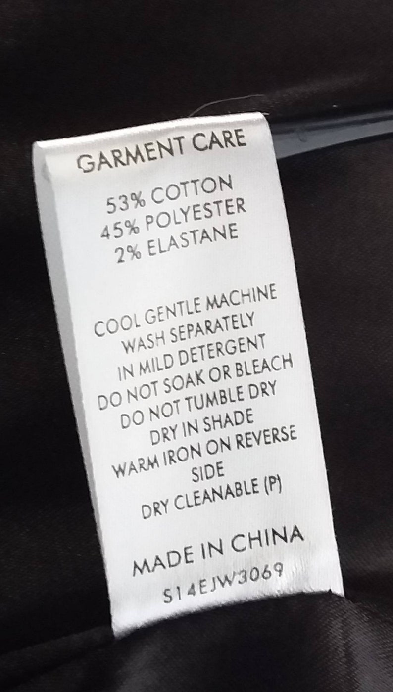 May include: A white garment care label with black text. The label states "GARMENT CARE" and lists the fabric composition as 53% cotton, 45% polyester, and 2% elastane. The label also includes instructions for washing, drying, and ironing the garment. The label states "MADE IN CHINA" and includes a product code: "S14EJW3069".