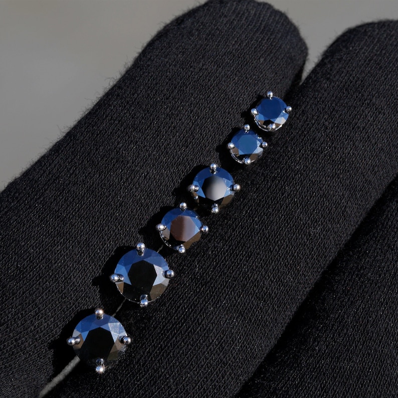 May include: A set of six black diamond earrings in various sizes, displayed on a black fabric background.