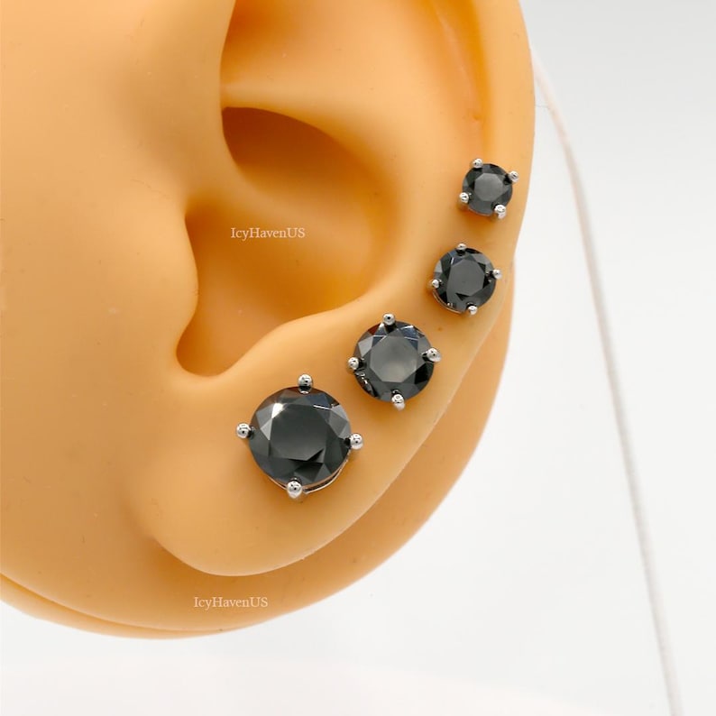 May include: Four black gemstone earrings of different sizes, set in silver, displayed on a model ear.