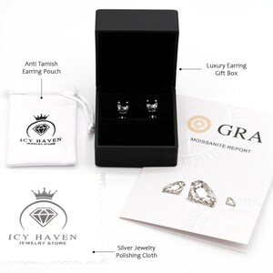 May include: A set of silver earrings with a square-shaped clear gemstone in a black gift box. The earrings come with a jewelry pouch, a polishing cloth, and a moissanite report.