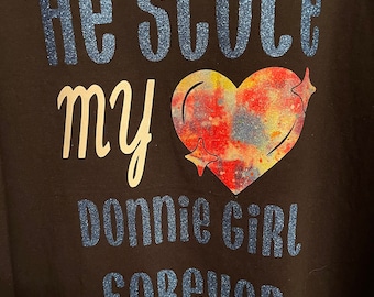 Könnte beinhalten: Schwarzes T-Shirt mit dem Text "He Stole My Donnie Girl Forever". Der Text "He Stole" und "Forever" ist in blauem Glitzer. Das Wort "my" ist in weißer Schrift. Eine farbenfrohe Herzgrafik befindet sich in der Mitte.