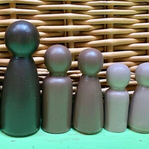 Puede incluir: Un conjunto de ocho muñecos de madera de diferentes tamaños y tonos de marrón, gris y blanco. Los muñecos están dispuestos en fila de mayor a menor, con el muñeco más grande a la izquierda y el más pequeño a la derecha.