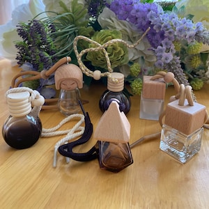 Könnte beinhalten: Sechs verschiedene Auto-Lufterfrischer mit Holzdeckeln und Glasflaschen. Die Flaschen sind mit verschiedenen farbigen Flüssigkeiten gefüllt. Die Lufterfrischer hängen an Schnüren mit Holzperlen.