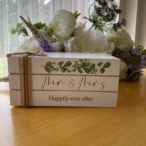 May include: White wooden box with a green leafy design and the text "Mr. & Mrs. Happily ever after".