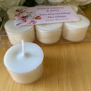 Puede incluir: Un juego de seis velas de té blancas sin aroma en un recipiente de plástico transparente. Las velas están dispuestas en dos filas de tres. El recipiente tiene una etiqueta que dice "Wicken Candles & Gifts" e incluye una dirección de sitio web y una dirección de correo electrónico.