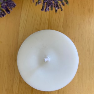 Peut inclure: Une bougie chauffe-plat ronde et blanche avec une m&egrave;che centrale. La bougie est pos&eacute;e sur une surface en bois brun clair, avec des brins de lavande violette et des fleurs blanches en arri&egrave;re-plan. Id&eacute;ale pour une ambiance relaxante.