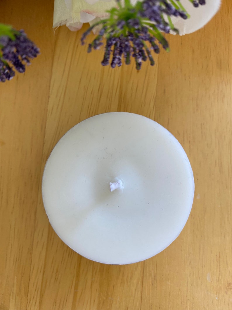 Peut inclure: Une bougie chauffe-plat ronde et blanche avec une m&egrave;che centrale. La bougie est pos&eacute;e sur une surface en bois brun clair, avec des brins de lavande violette et des fleurs blanches en arri&egrave;re-plan. Id&eacute;ale pour une ambiance relaxante.