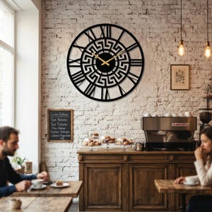 Large Meander metal wall clock featuring an ancient Greek key pattern, modern black steel wall art decor hanging on a rustic brick wall in a cozy cafe setting.