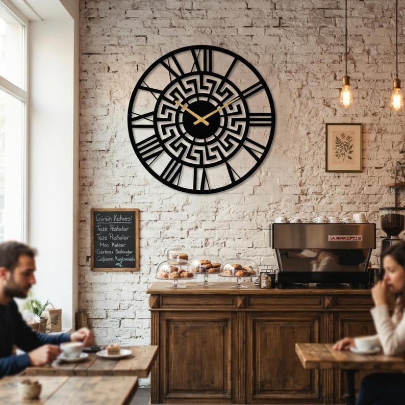 Large Meander metal wall clock featuring an ancient Greek key pattern, modern black steel wall art decor hanging on a rustic brick wall in a cozy cafe setting.