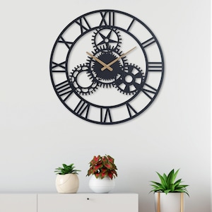 May include: Black metal wall clock with Roman numeral markings and a gear design. The clock has gold-colored hands and is hanging on a white wall.
