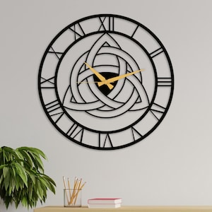 May include: Black metal wall clock with Roman numeral markings and a gold-colored hour and minute hand. The clock face features a Celtic knot design.