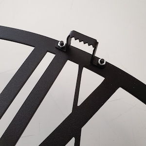 "Close-up detail of hanger on the back side of a black metal wall clock.