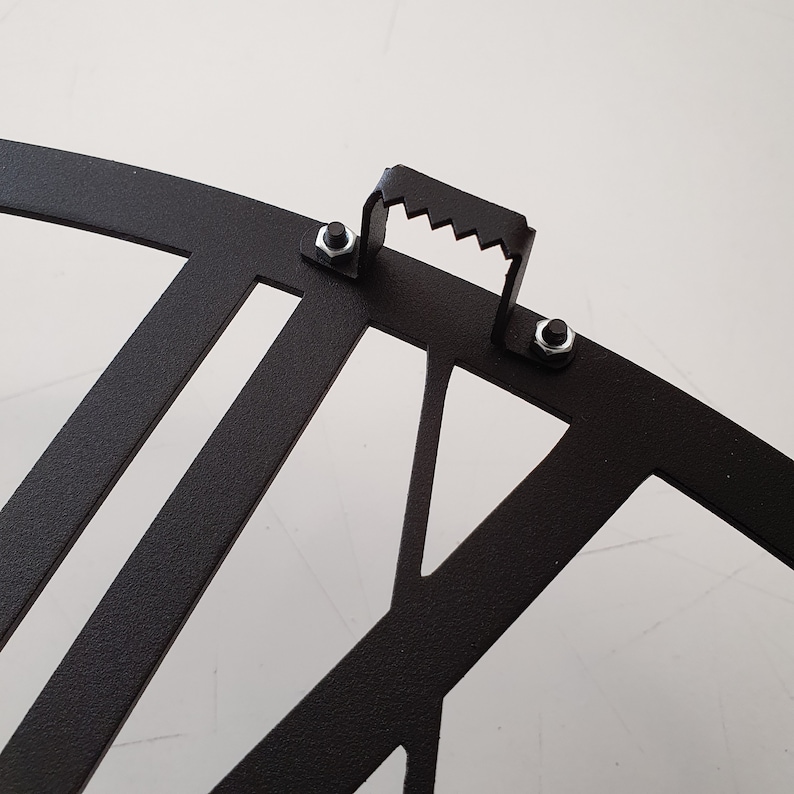 "Close-up detail of hanger on the back side of a black metal wall clock.
