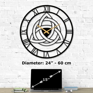 Size guide infographic for Metal Wall Clock with Triquetra design on a white brick wall. Image text shows 'Diameter:  24 inch - 60 cm' compared to a 15-inch laptop on a desk.
