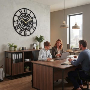 Large Meander metal wall clock featuring an ancient Greek key pattern, modern black steel wall art decor hanging above a desk in a professional contemporary office meeting room.