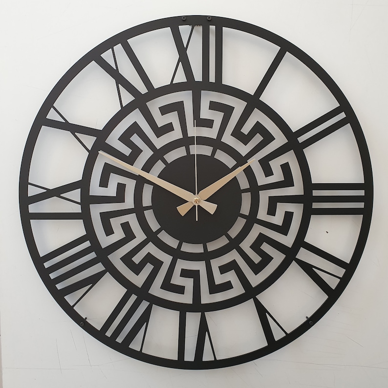 Close up photo of black metal wall clock featuring an intricate ancient Greek key pattern and Roman numeral dial, modern laser-cut steel wall art decor.