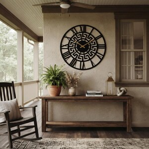 Large Meander metal wall clock with an ancient Greek key pattern, stylish black steel wall art decor displayed on a rustic farmhouse porch.