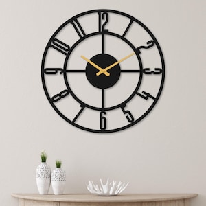 Könnte beinhalten: Schwarze Wanduhr aus Metall mit goldfarbenen Zeigern und römischen Ziffern. Die Uhr hat ein großes, kreisförmiges Design mit einem schwarzen Zentrum.