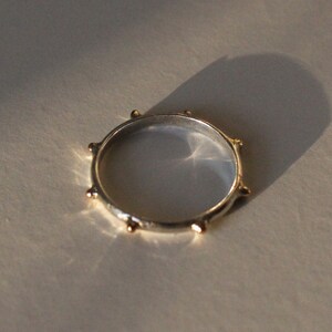 May include: A silver ring with gold accents around the band. The ring has a simple design with small, round gold accents.