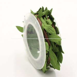 May include: A spool of brown twine wrapped with green fabric leaves. The leaves are sewn together to create a garland.