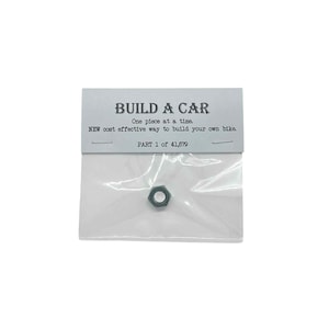 以下が含まれることがあります： 「BUILD A CAR」キットの一部である小さな六角ナットが、透明なビニール袋にパッケージされています。「BUILD A CAR」と「One piece at a time」と書かれたカードが付属しています。「PART 1 of 41,679」とも書かれています。