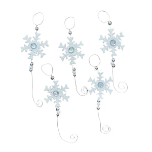 May include: Five white snowflake ornaments with silver wire and beads hanging from a white background. Each snowflake has a silver glitter finish and a clear rhinestone in the center.