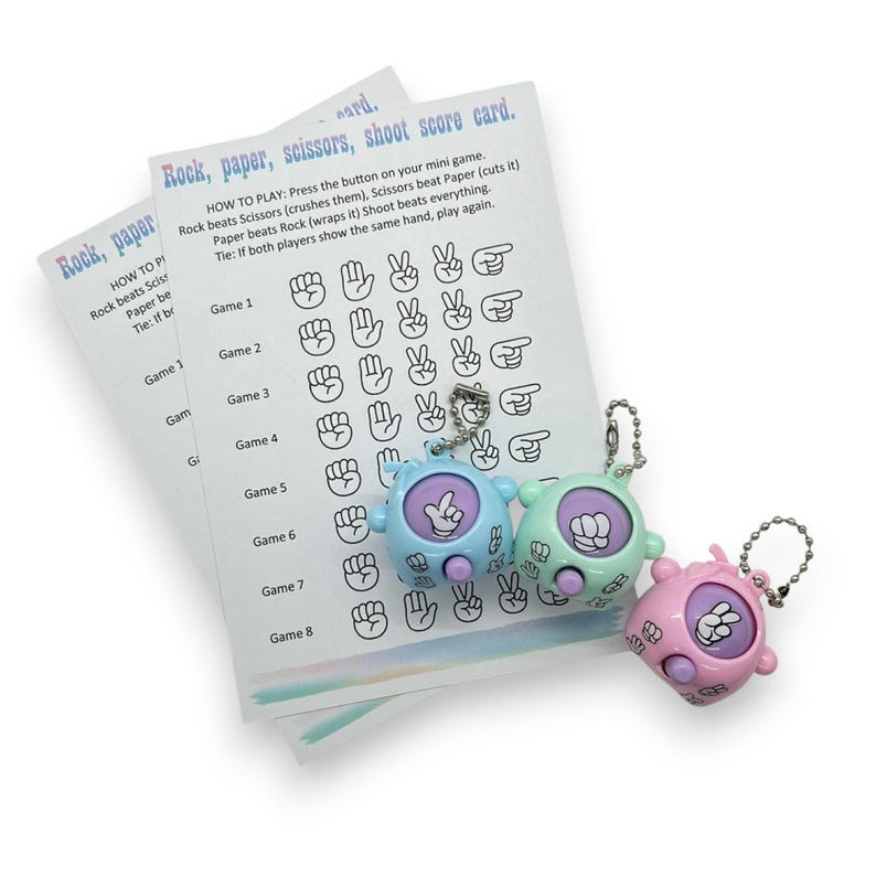May include: Three mini Rock, Paper, Scissors game keychains in blue, green, and pink, with a matching score card. The keychains have a button to display the hand signs. The score card has the rules and game results.