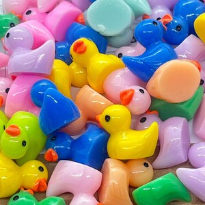 Może przedstawiać: Kolekcja małych, kolorowych plastikowych figurek kaczek i ptak&oacute;w. Kaczki są ż&oacute;łte, r&oacute;żowe i niebieskie. Ptaki są zielone, r&oacute;żowe i niebieskie. Figurki mają około 2,5 cm wysokości.