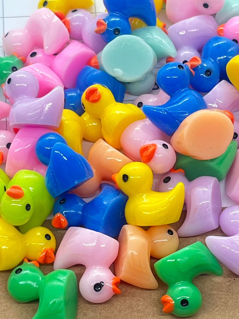 Może przedstawiać: Kolekcja małych, kolorowych plastikowych figurek kaczek i ptak&oacute;w. Kaczki są ż&oacute;łte, r&oacute;żowe i niebieskie. Ptaki są zielone, r&oacute;żowe i niebieskie. Figurki mają około 2,5 cm wysokości.