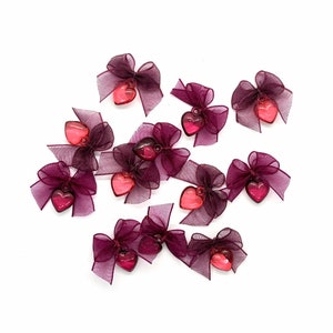Puede incluir: Encantos en forma de corazón de color burdeos y rosa con lazos. Los encantos están hechos de plástico y tienen un acabado brillante.