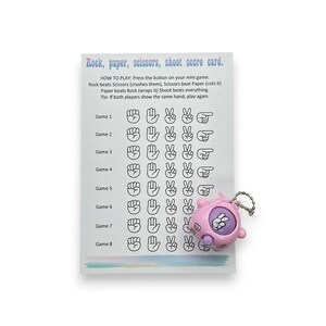 May include: A score card for the game Rock, Paper, Scissors, Shoot. The card has instructions and a game chart. A pink mini game with a keychain is attached to the card. The text on the card reads "Rock, paper, scissors, shoot score card."