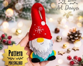Op de afbeelding: Een handgemaakte kerstkabouterornament met een rode hoed, witte baard en turquoise lichaam. De hoed heeft een wit sneeuwvlokontwerp. De afbeelding bevat de tekst "My Little Art Designs" en "Pattern PDF|SVG|DXF".