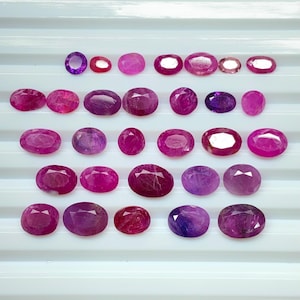 May include: A collection of oval-shaped gemstones in shades of red and purple. The gemstones are displayed in rows, highlighting their different sizes and colours, from deep ruby to light amethyst.