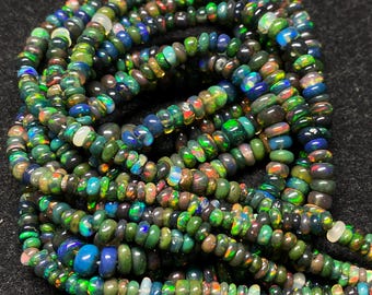 May include: Strands of colorful opal beads. The beads display a mix of colors, including green, blue, orange, and white. The beads are small and round, and appear to be strung together. The background is black.