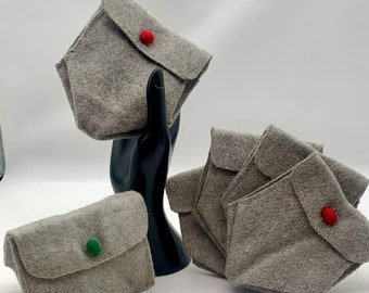 May include: Five grey felt pouches with red and green buttons. The pouches are folded and arranged on a black surface.