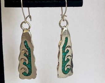 May include: A pair of silver dangle earrings with turquoise inlay. The earrings feature a leaf-like design with a silver hook.