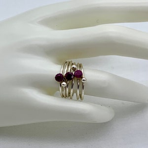 May include: A silver ring with multiple bands and purple gemstones. The ring is designed with a cluster of three gemstones in the centre.